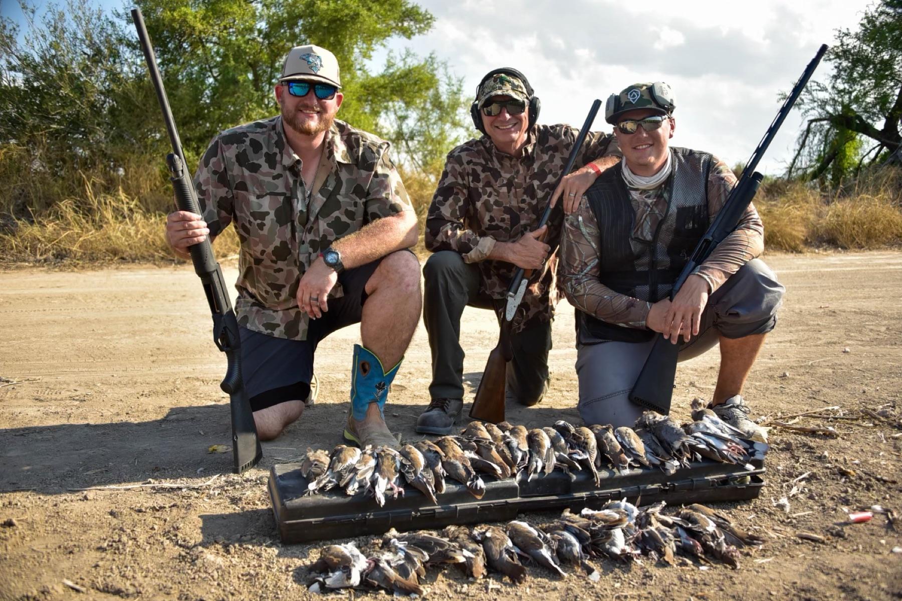 Three hunters kneeling behind their doves at the field edge